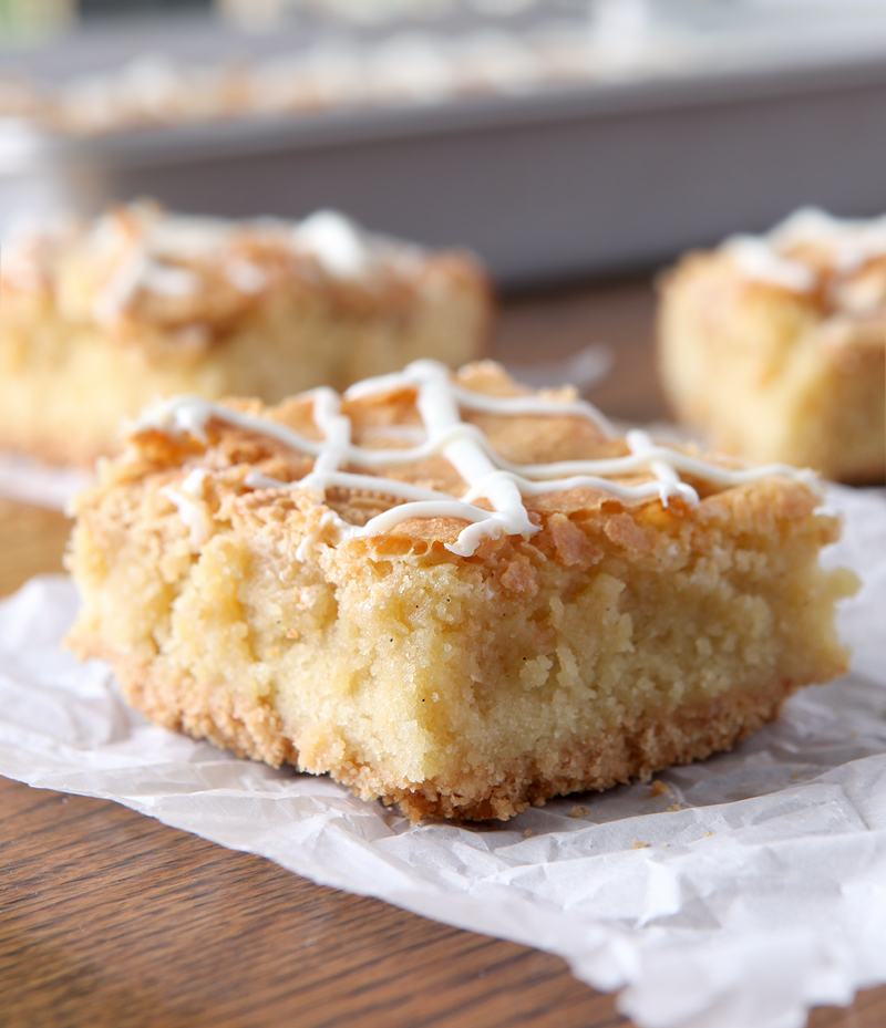 Close up of a layered vanilla bar, with the tender blondie middle clearly visible, along with tiny flakes of vanilla bean.