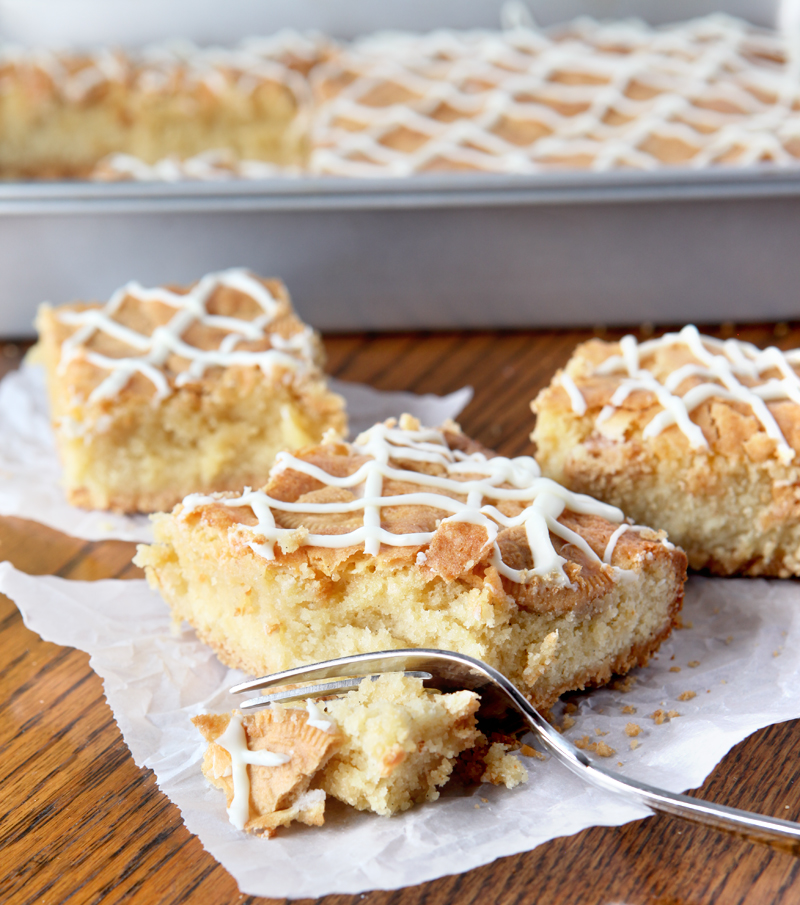 Three squares of ooey gooey vanilla bars sit atop crinkled pieces of parchment paper.