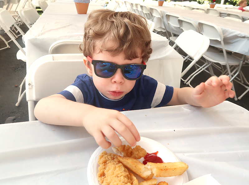 toddler with sunglasses eating chicken and fries