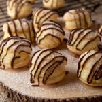 A simple pate a choux dough cream puff recipe filled with a light orange pastry cream and drizzled with chocolate. Chocolate drizzled orange cream puffs are a delightful dessert that's not too heavy!