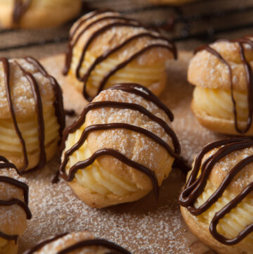 A simple pate a choux dough cream puff recipe filled with a light orange pastry cream and drizzled with chocolate. Chocolate drizzled orange cream puffs are a delightful dessert that's not too heavy!