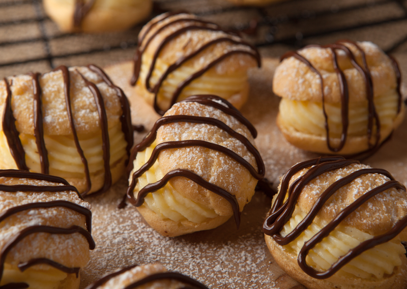 Close up of  French cream puffs with a light orange pastry cream filling and a pretty chocolate drizzle.