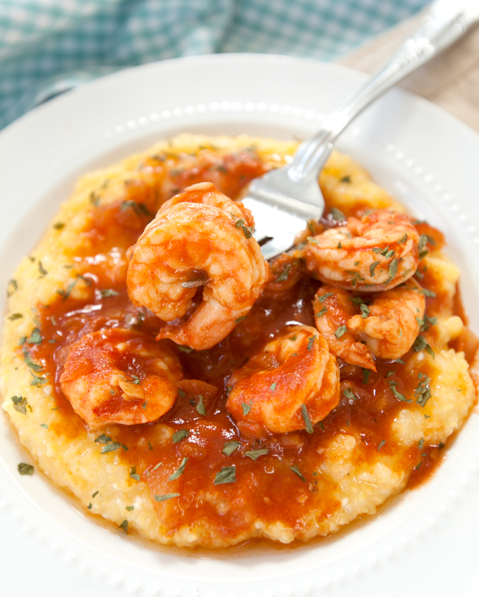 A close up of bloody mary shrimp and grits, with a fork scooping up a tender piece of cooked shrimp.