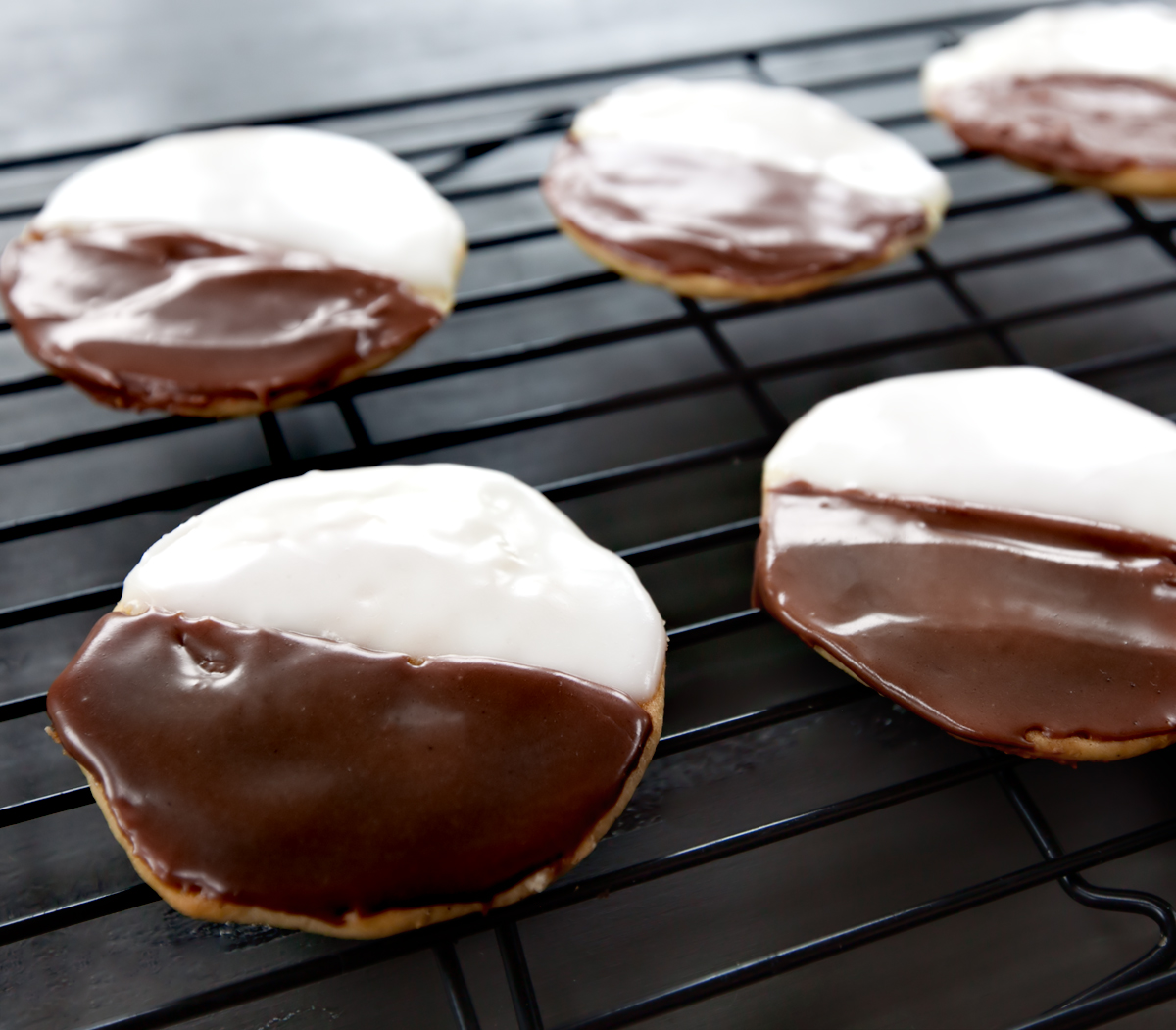 A cooling rack of a finished half moon cookie recipe with shiny icing.