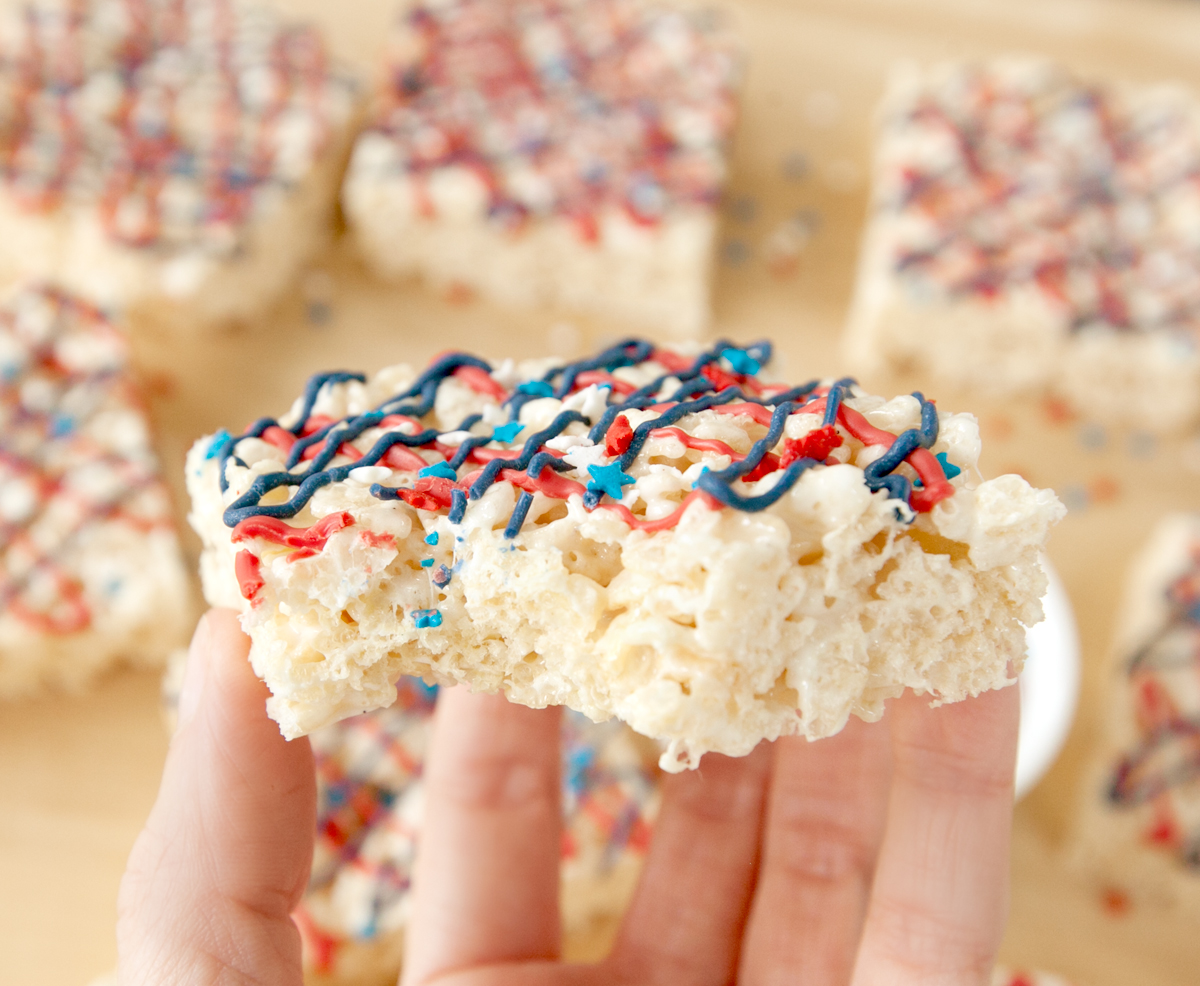 hand holding a red white and blue rice krispie treat with a bite taken out