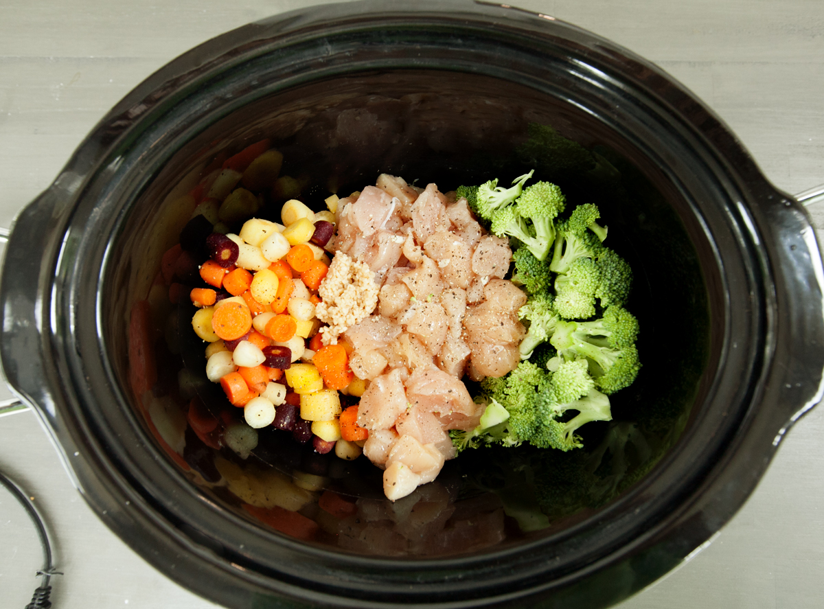 colorful ingredients for crock pot chicken and biscuits in a black crock pot