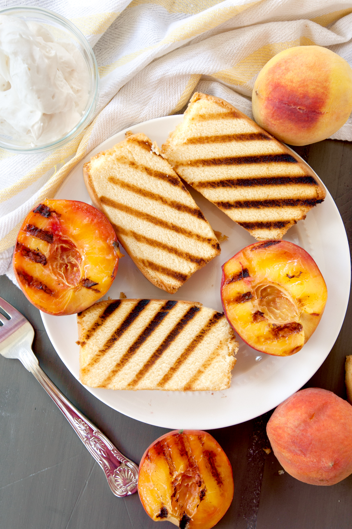 overhead photo of a plate of grilled pound cake slices and grilled peaches with a bowl of whipped cream.