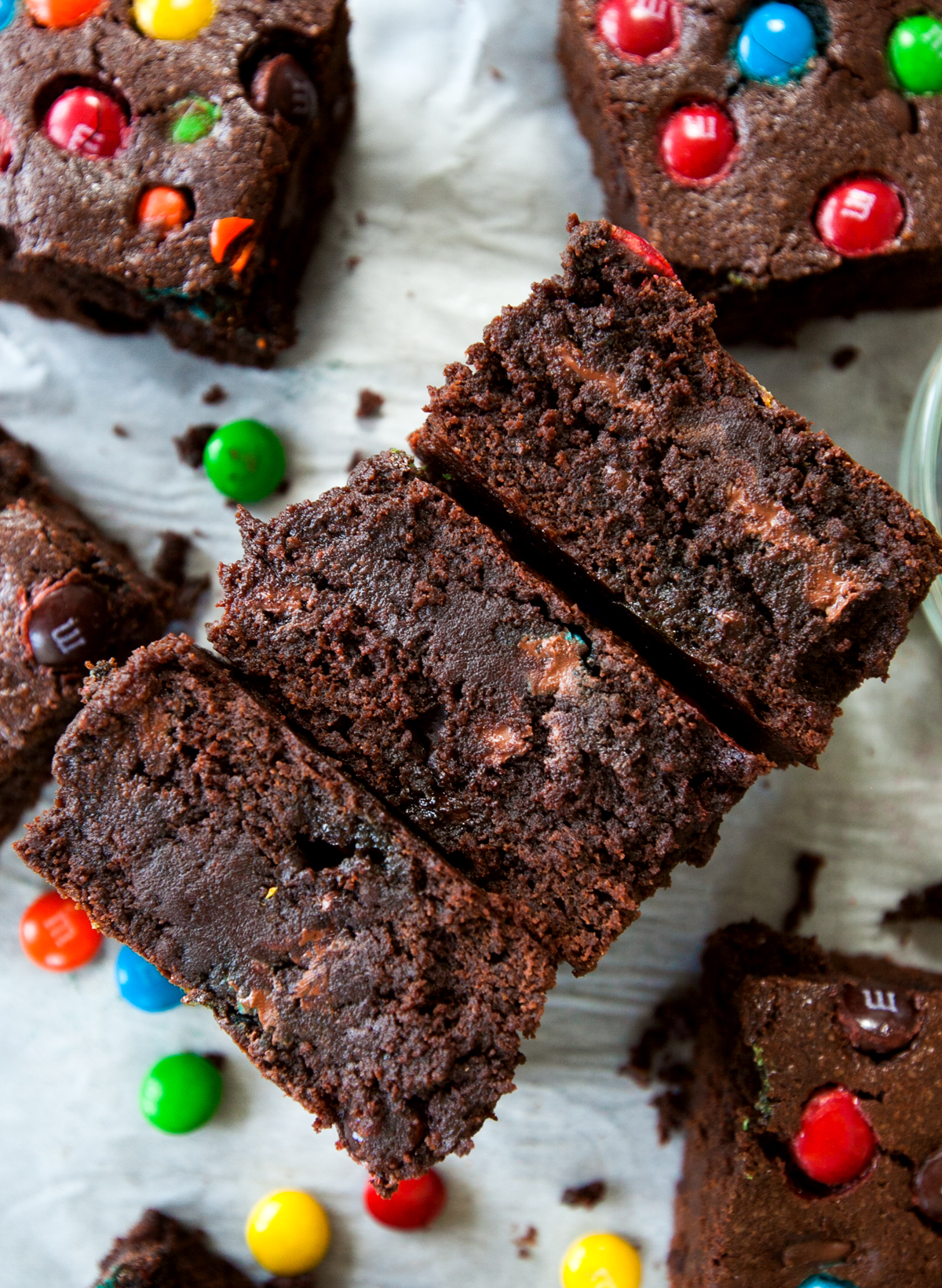 Cross section of three thick M&M fudge brownies with melty chocolate seen throughout.