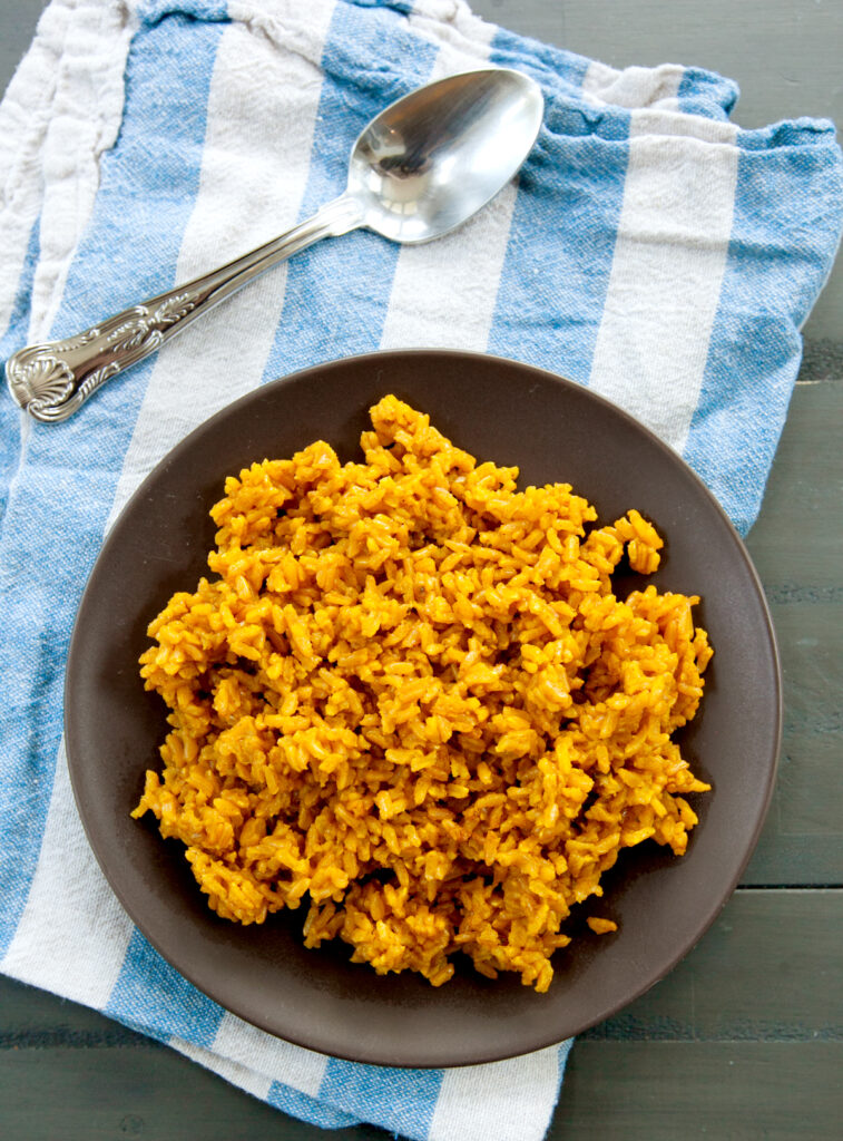 an overhead view of a plate of turmeric rice on a blue and white dish towel with a spoon nearby