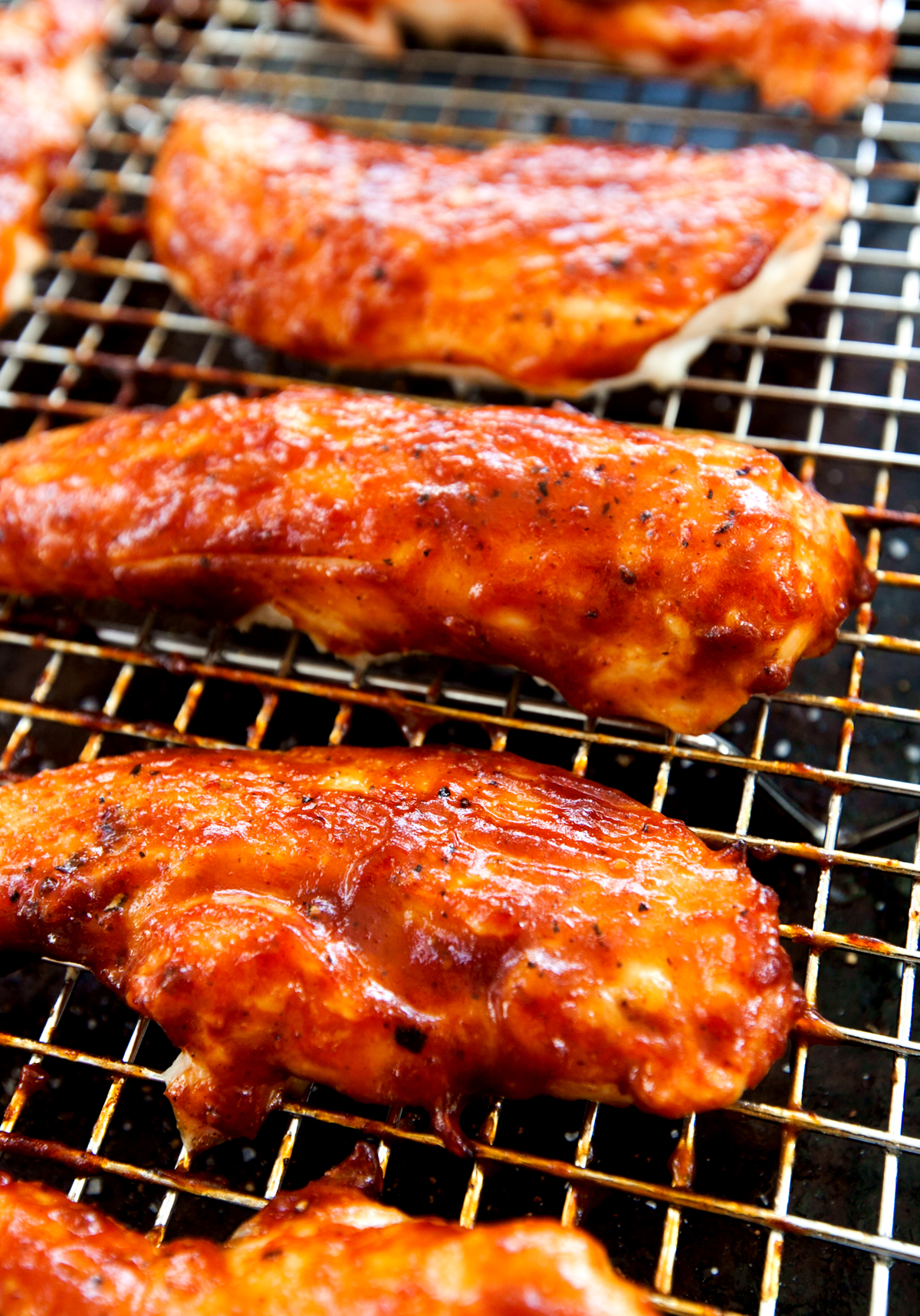 A close up view of juicy caramelized baked BBQ chicken tenders with spicy barbecue sauce.