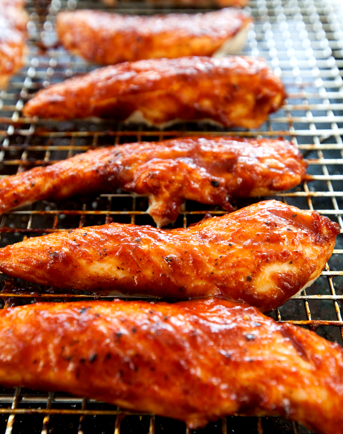 Juicy caramelized baked BBQ chicken tenders lined up on a rack.