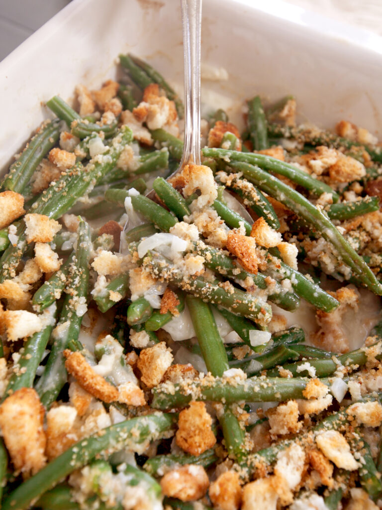 A dish of green bean casserole without mushroom soup with a large stainless steel spoon inside.
