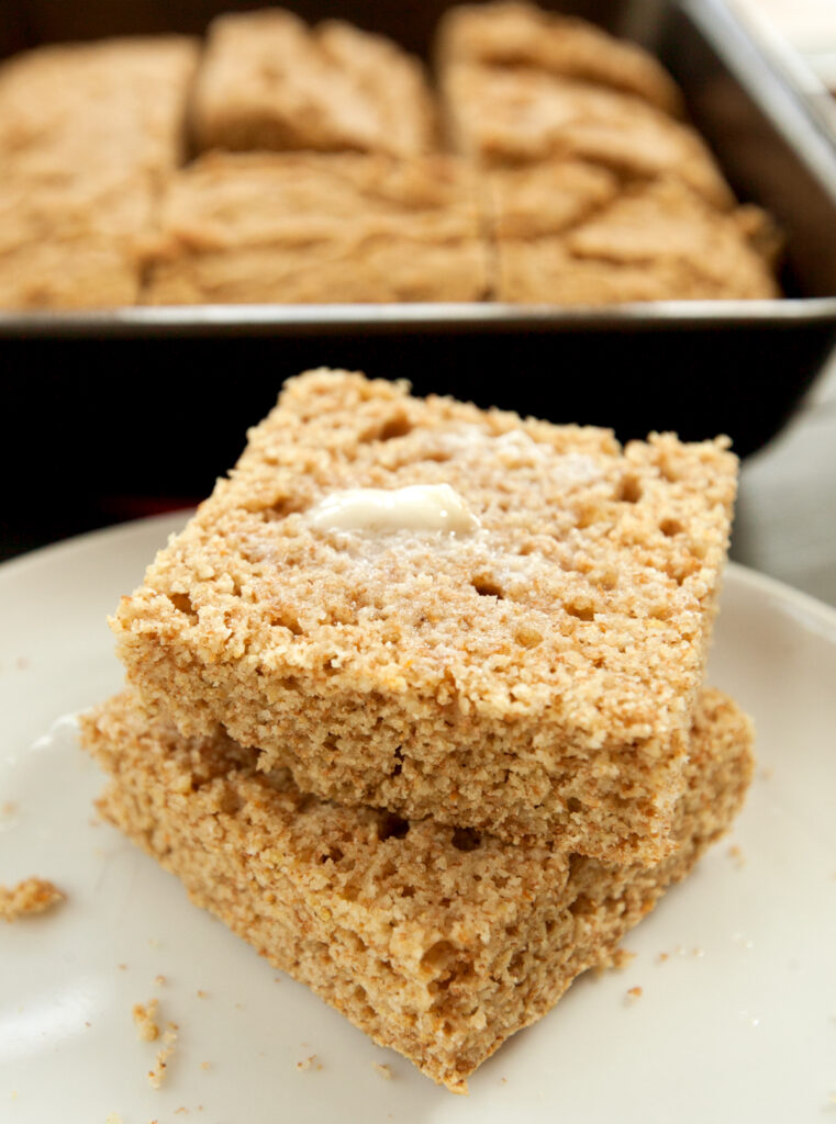 A stack of healthy cornbread slices smeared with a pat of butter.