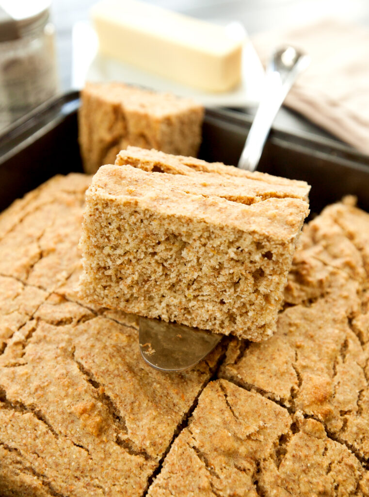 A thick slice of healthy cornbread rests on top of the rest of the pan.