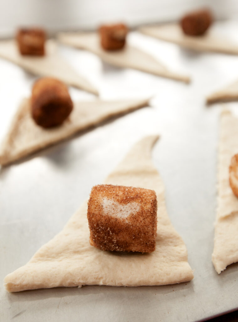 A cinnamon sugar coated marshmallow sitting on a piece of raw crescent roll dough.