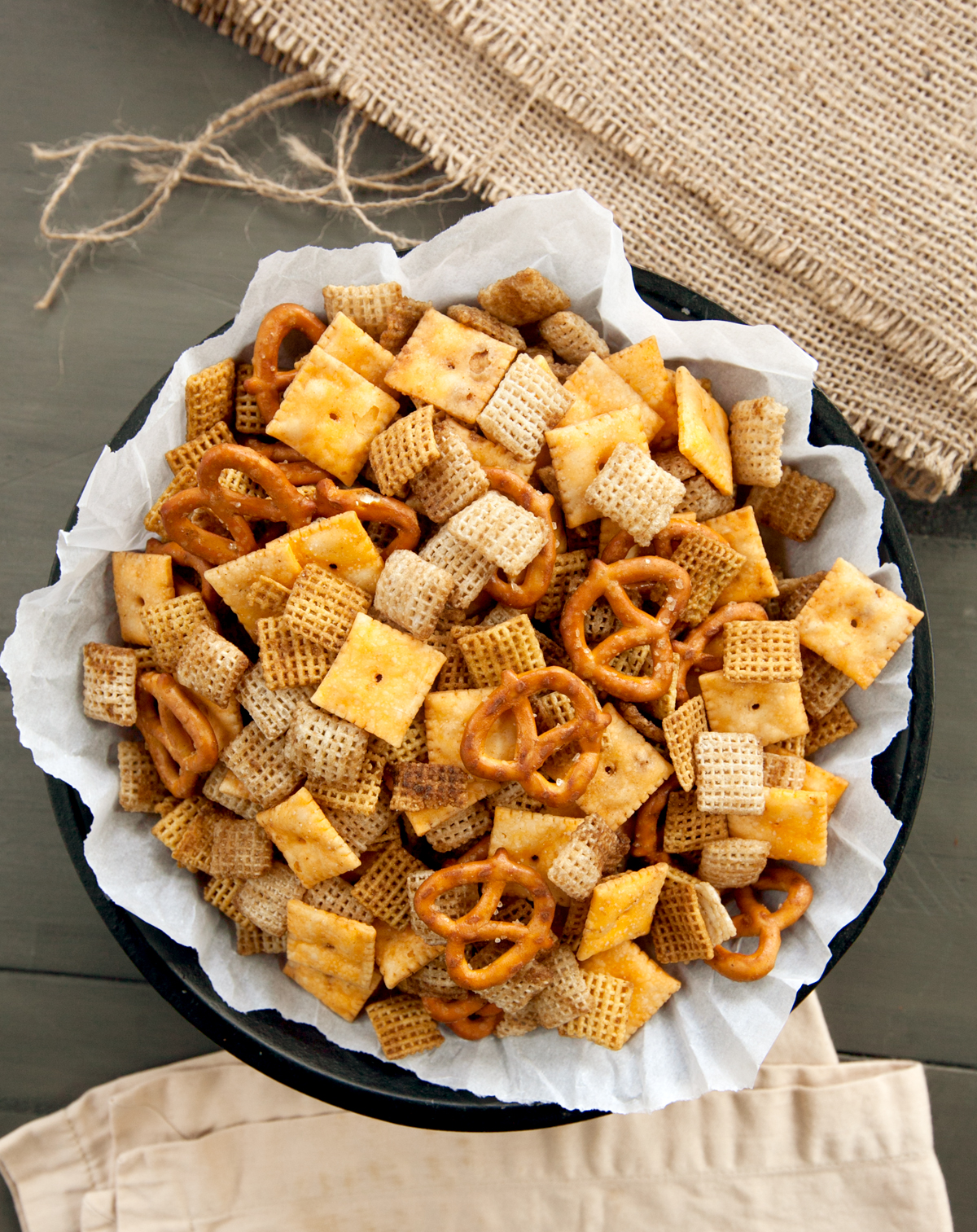 Overhead view of a bowl of bold Chex mix with burlap and neutral colored napkins