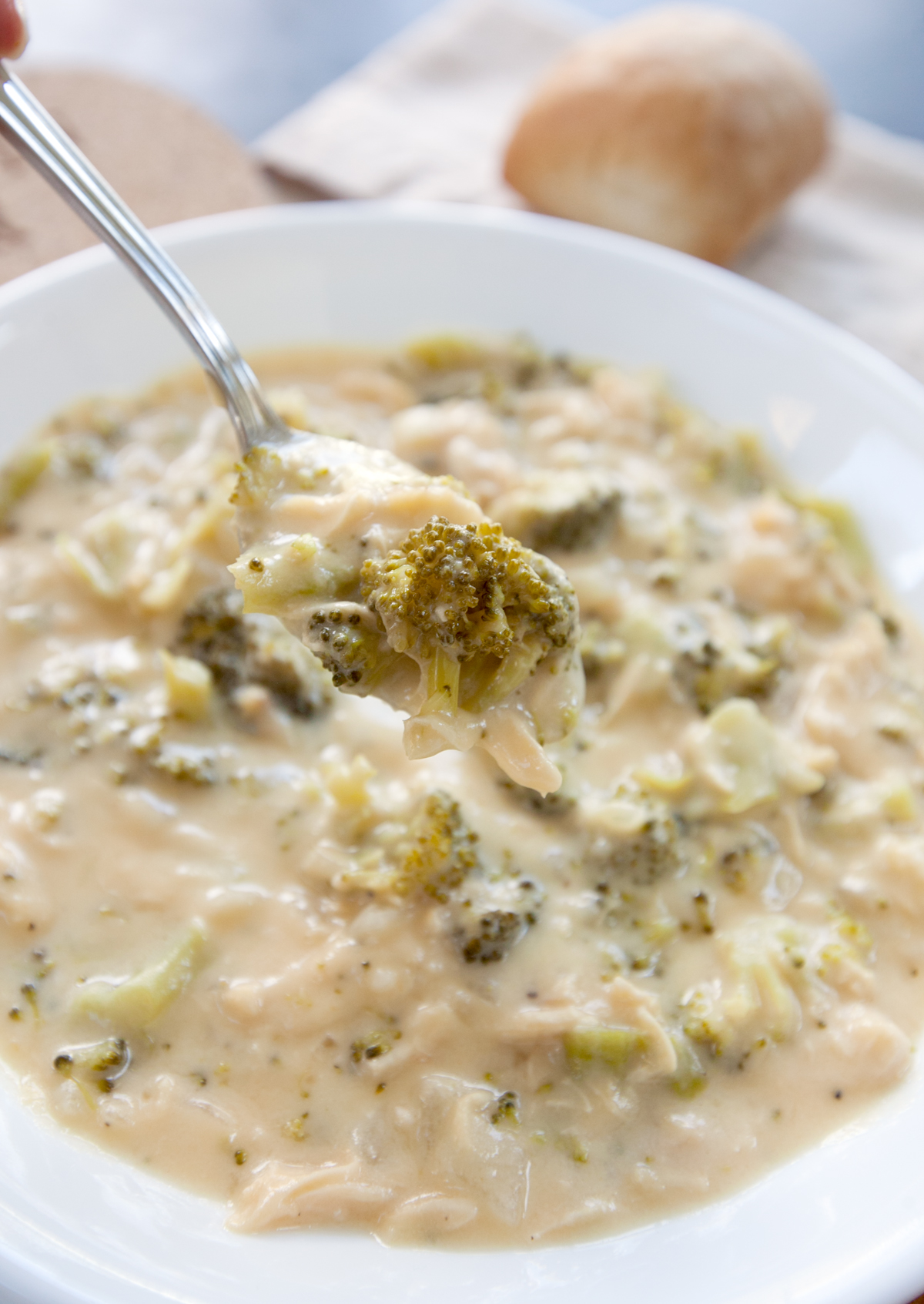 A spoon of chicken broccoli cheddar soup being lifted out of a bowl.