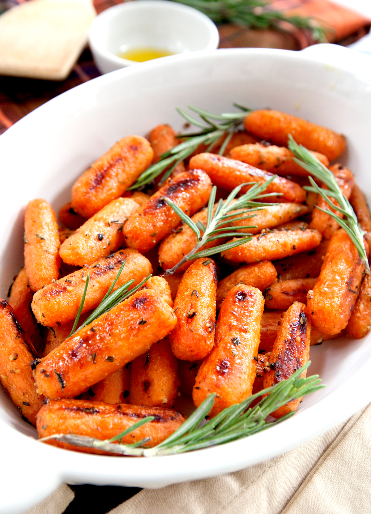 A dish of roasted rosemary carrots glistening with olive oil and bits of caramelized brown sugar and fresh sprigs of rosemary.