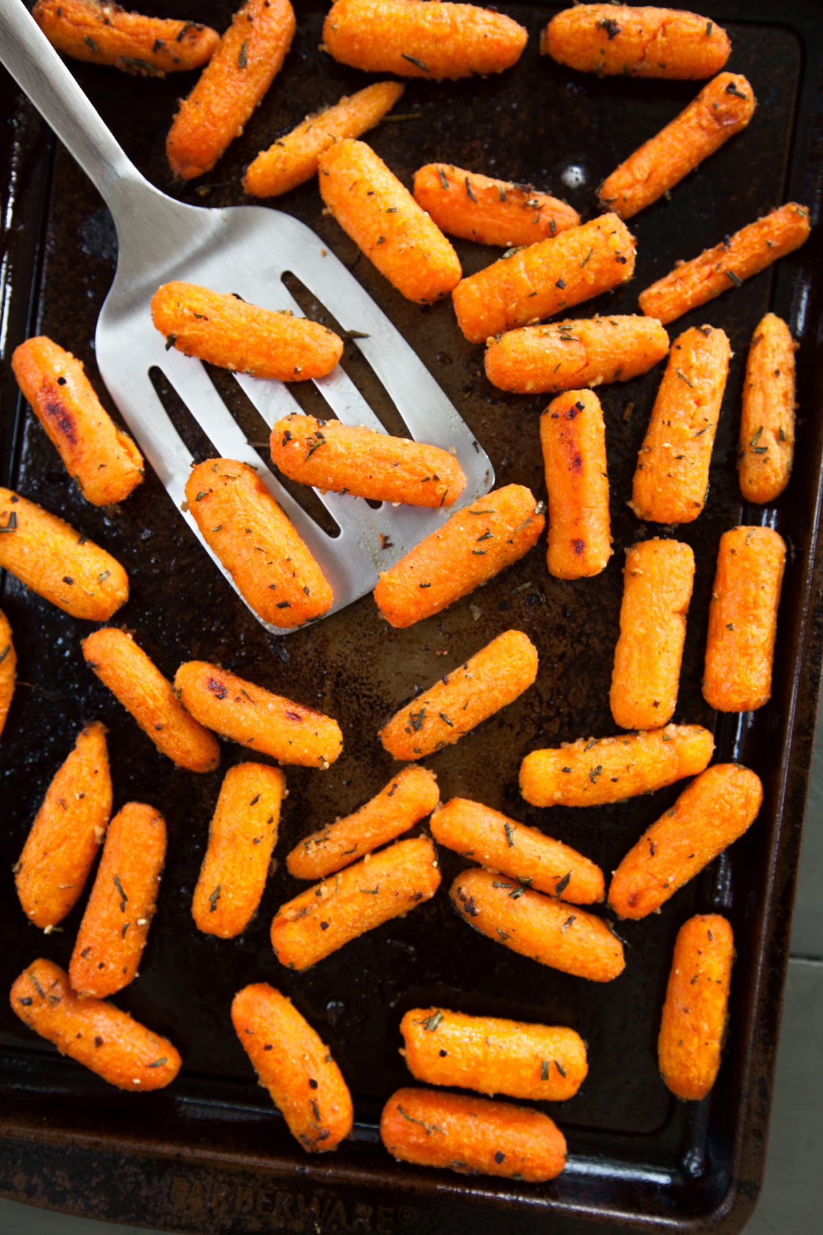 Overhead view of a baking sheet of roasted baby carrots with sprinkles of rosemary.