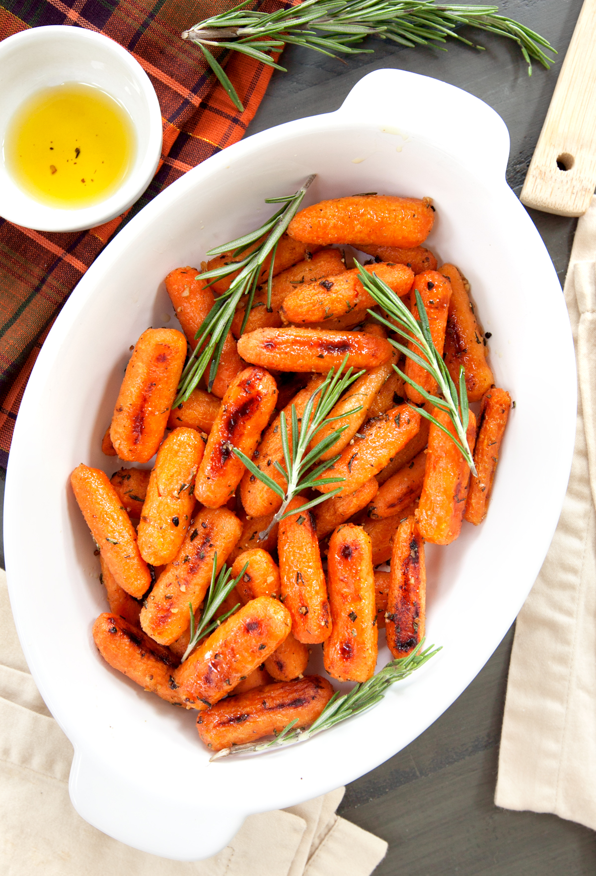 An overhead view of a white dish of roasted rosemary carrots with fresh sprigs of rosemary.