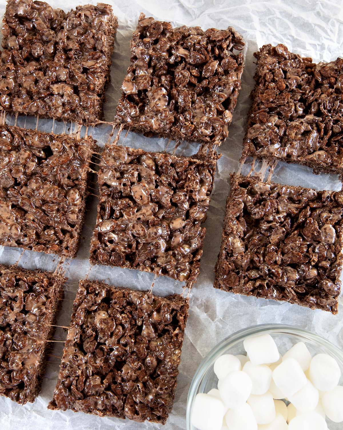  Overhead view of squares of cocoa pebbles treats with gooey marshmallow  tendrils in between.