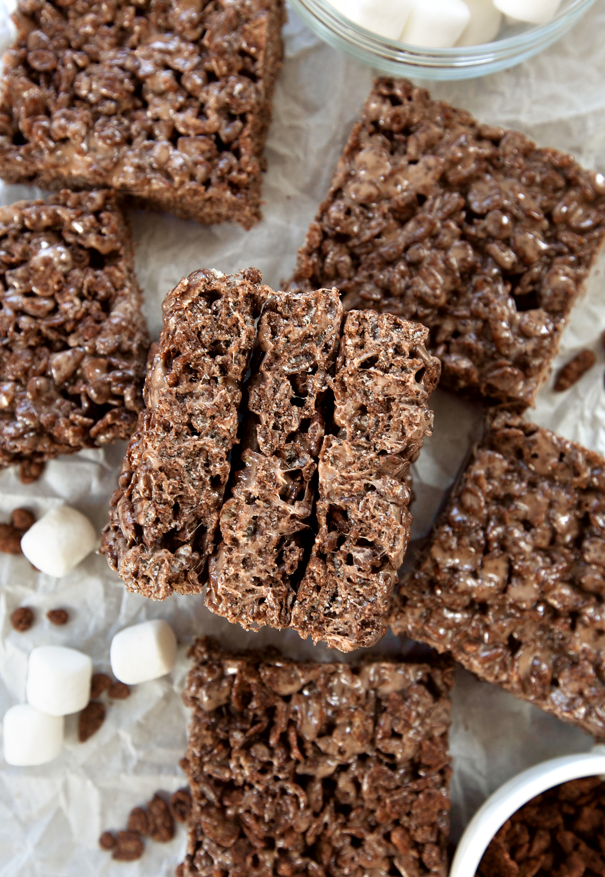 A cross section of three cocoa pebbles treats with marshmallows and cereal scattered around