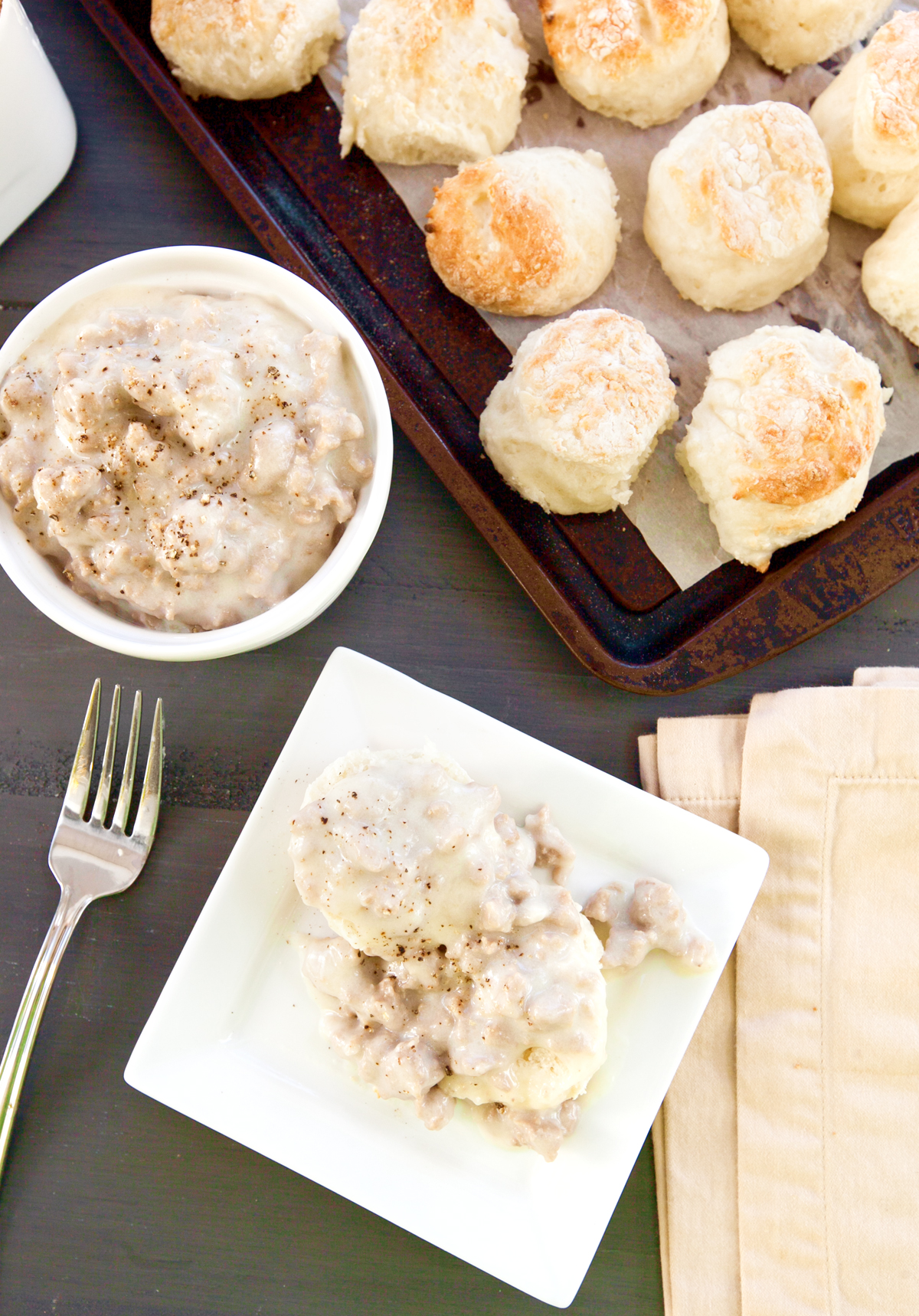 An overhead view of turkey sausage gravy spooned over some biscuits, with a tray of low calorie biscuits in the background.
