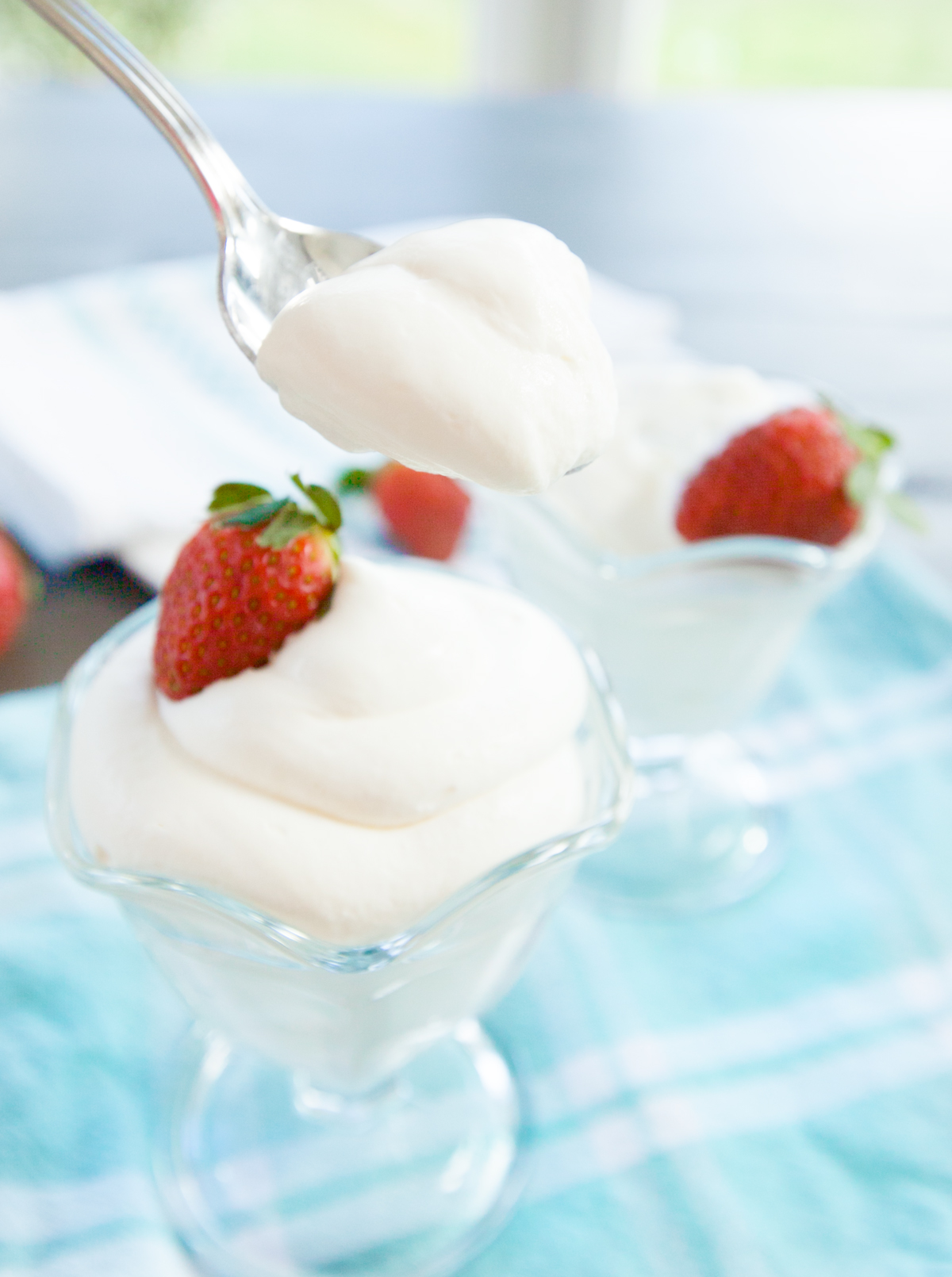 a spoon lifting a bite of cream cheese mousse out of a dish that is garnished with a strawberry.