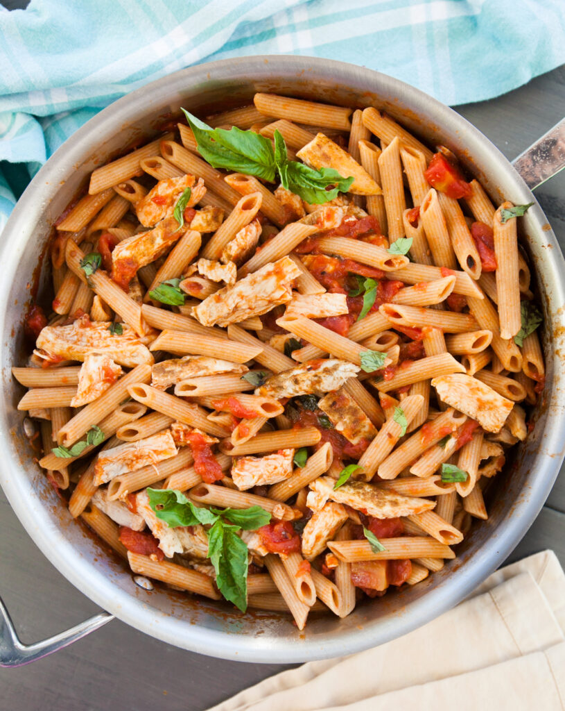 A saute pan containing a finished spicy chicken pasta recipe, garnished with additional fresh basil leaves.