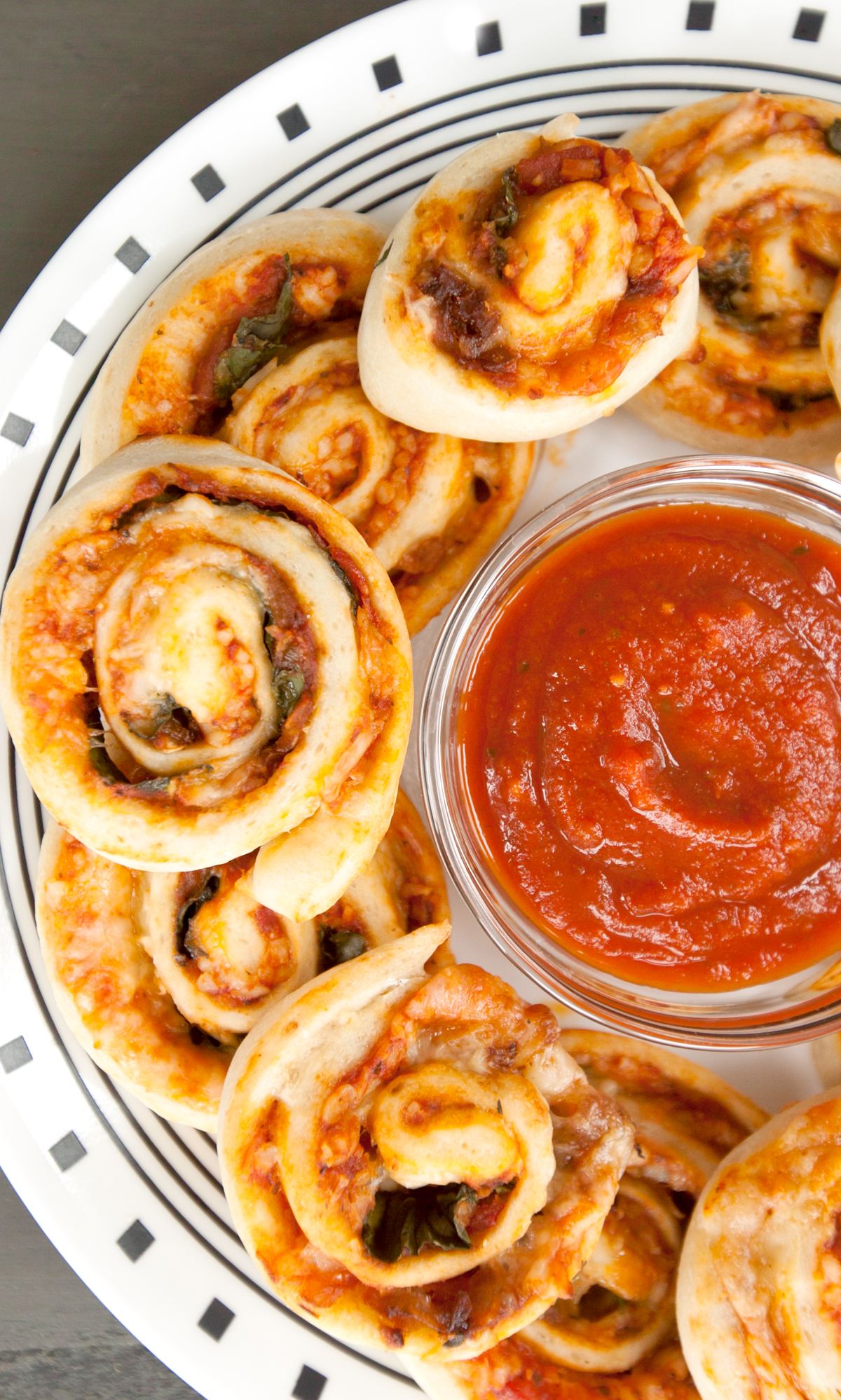 Vegetarian pizza rolls arranged on a plate next to a dipping cup of marinara sauce