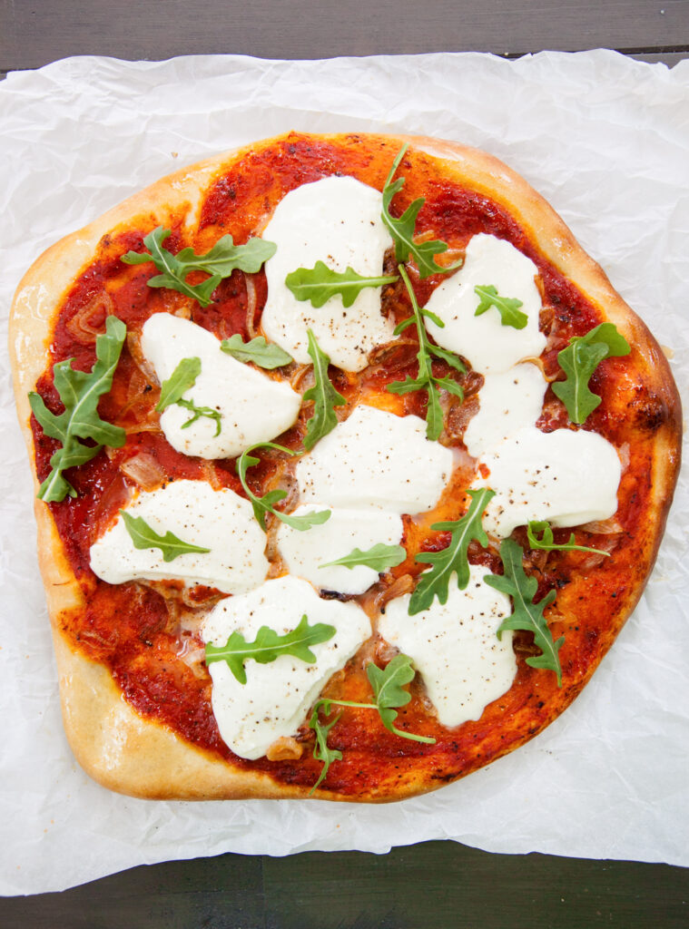 Overhead view of burrata pizza with a browned blistered crust and fresh arugula.