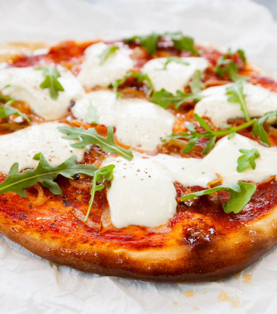 Close up of a crispy burrata pizza with melted burrata and fresh arugula.