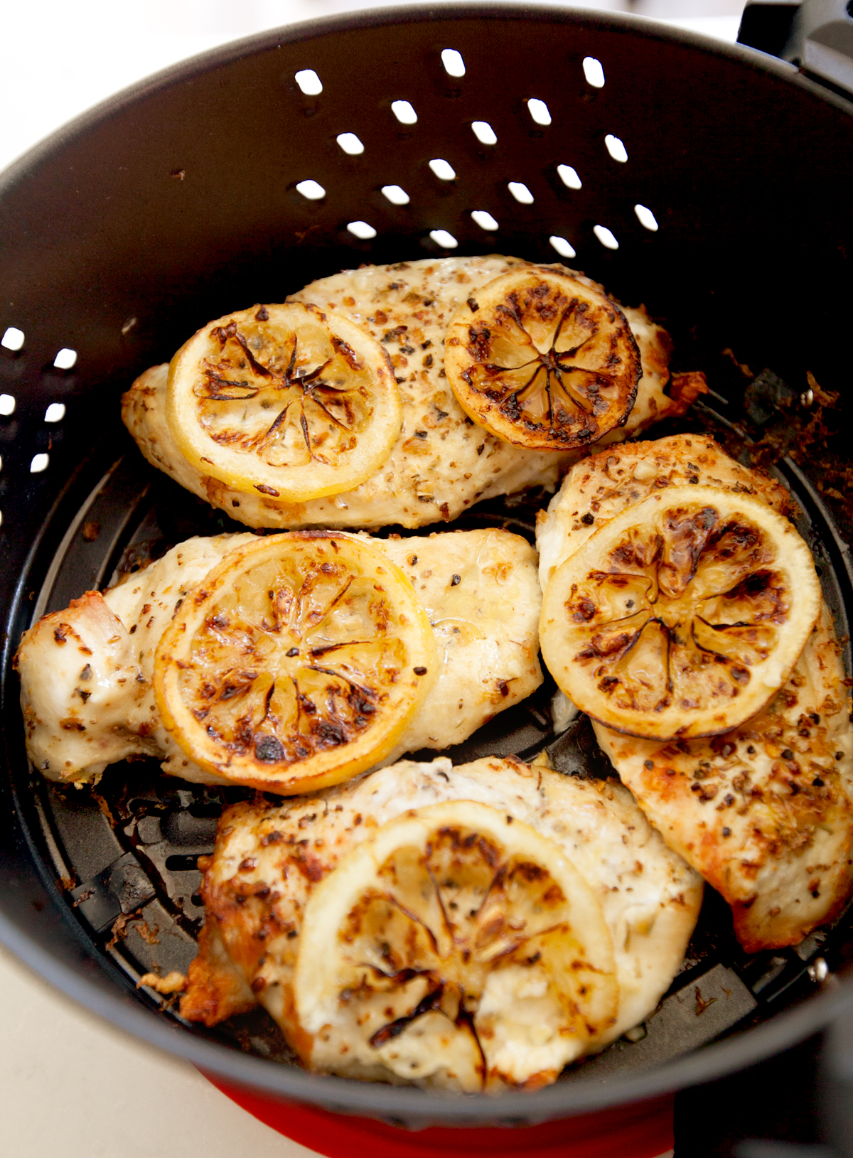 chicken breasts topped with lemon pepper and lemon slices in an air fryer basket.