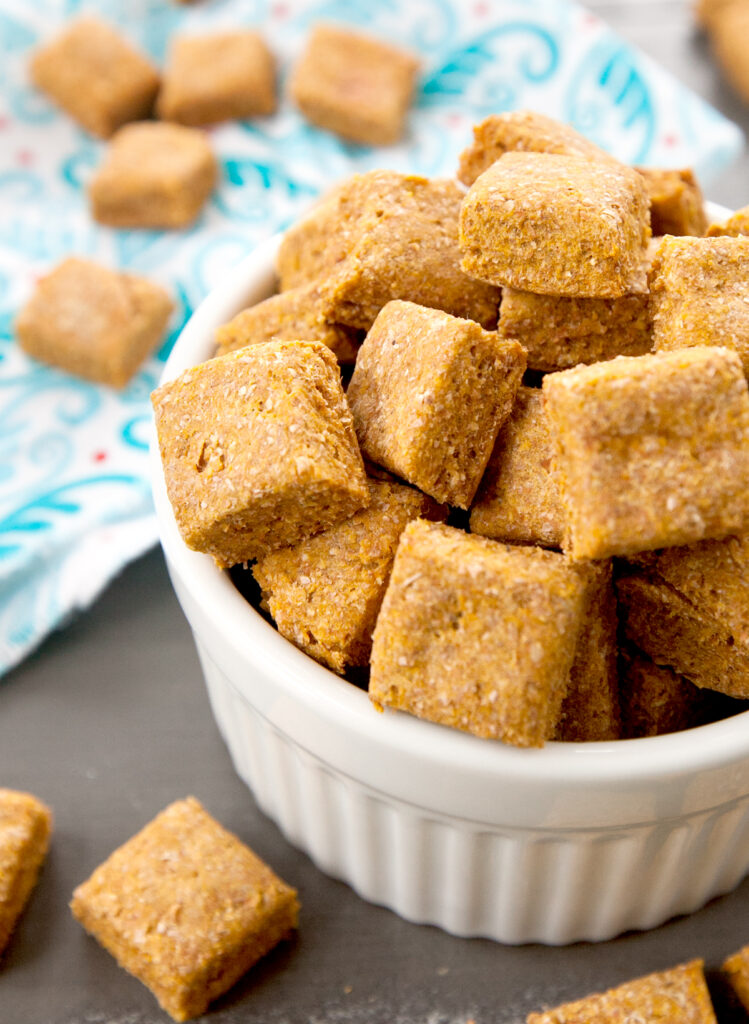 Close up of a bowl of homemade dog treats with some overflowing onto the table.