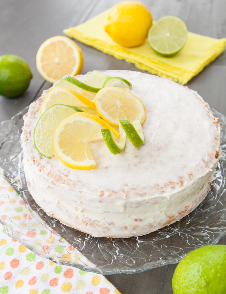 A whole sprite cake half-dressed with frosting and decorated with lemon and lime slices.