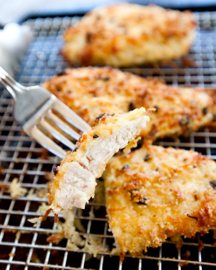 A fork taking a bite out of a chicken breast crusted with parmesan keto-friendly breading.