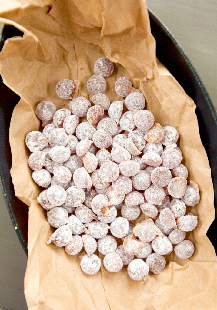 A pile of small dusted honey balls on a piece of crinkled parchment paper.