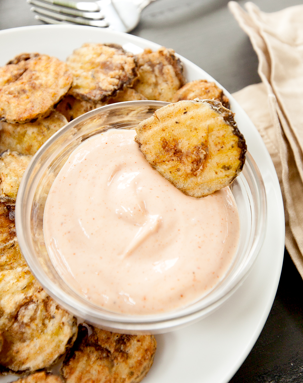 a crunchy fried pickle chip dipped into a glass bowl of cajun dipping sauce.