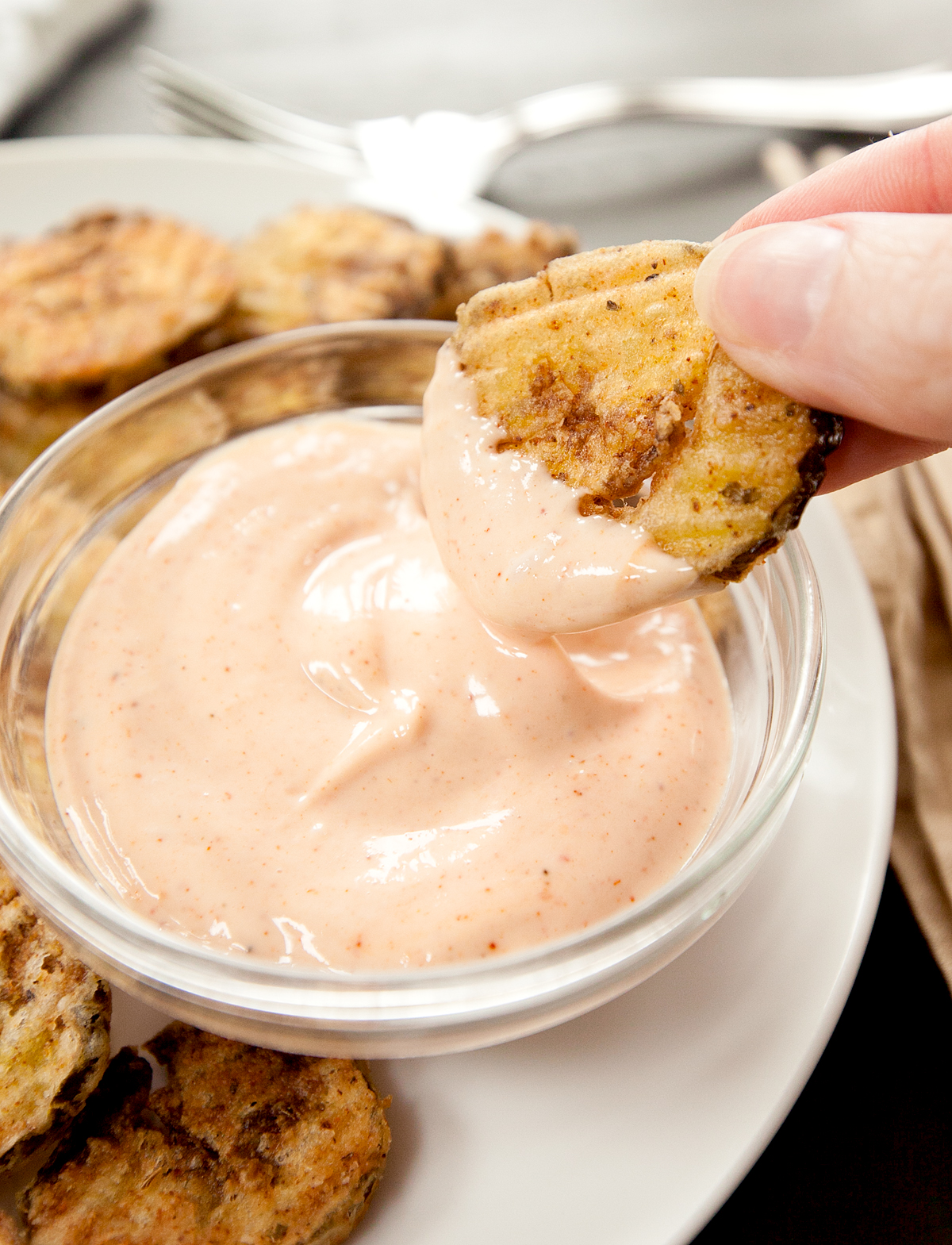 a deep fried pickle chip being dipped into cajun dipping sauce