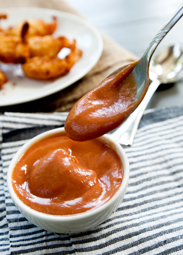 A small pinch bowl of cocktail sauce made without horseradish and being dipped with a spoon.