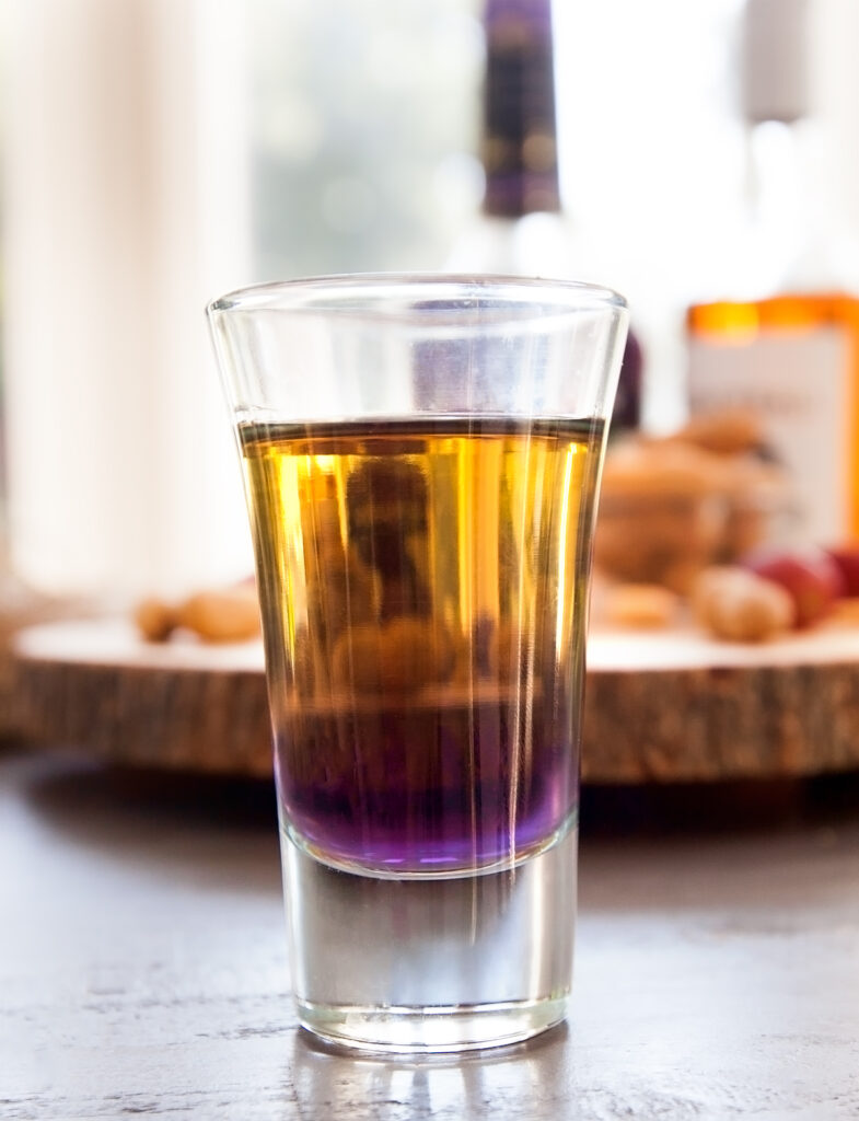 Close up of a layered peanut butter and jelly shot with golden and purple colors.