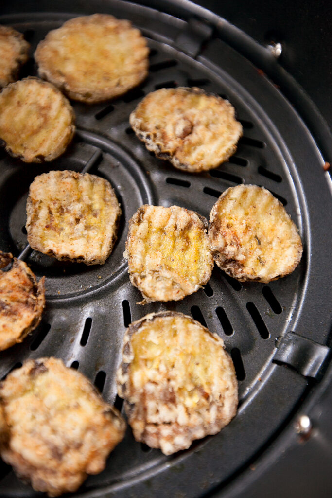 A layer of fried pickles in the basket of an air fryer.