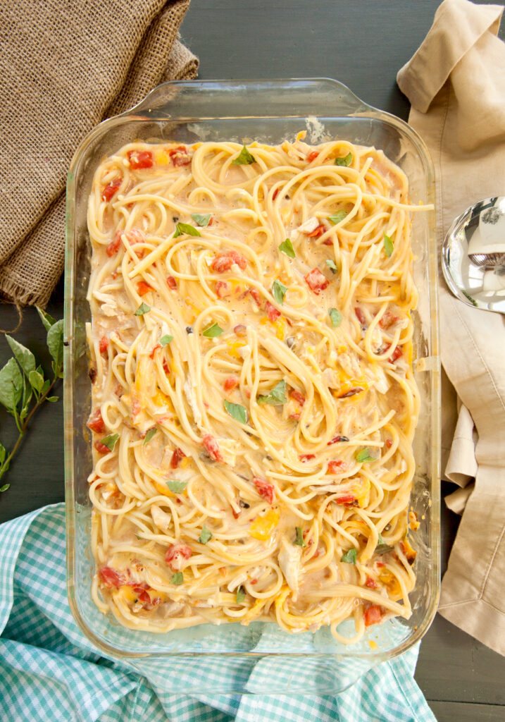 Overhead view of a rotel chicken spaghetti casserole garnished with torn basil leaves.