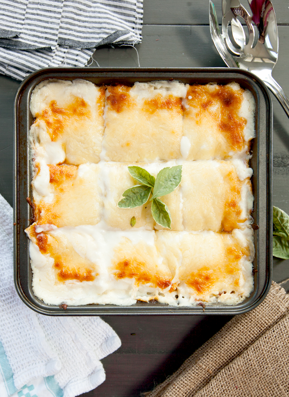 Overhead view of a vegetable lasagna with white sauce garnished with basil leaves.