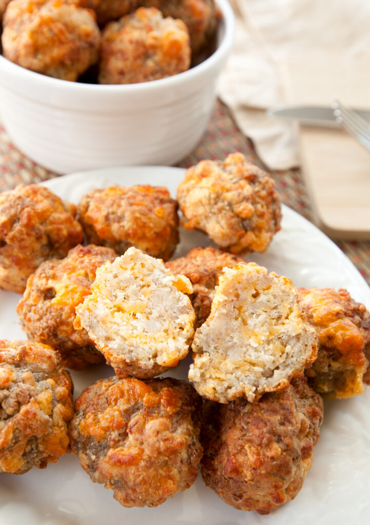 A pile of sausage balls with one sliced open, the cheesy inside visible.