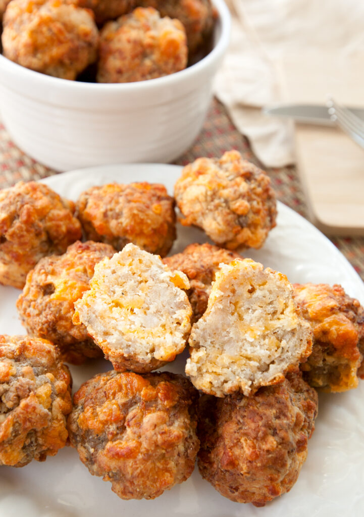 A pile of  sausage balls with one sliced open, the cheesy inside visible.