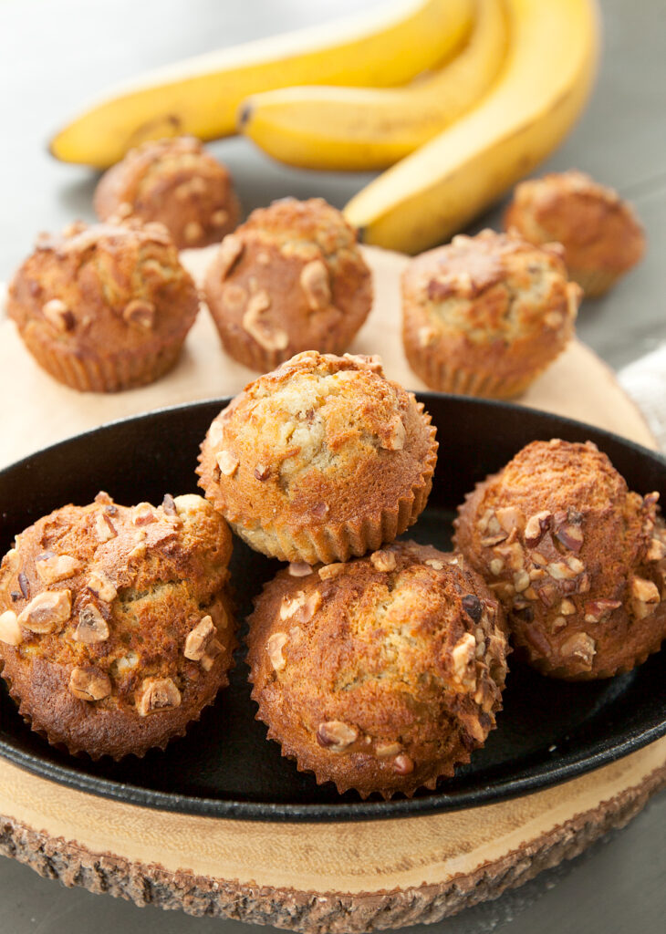 A cast iron bowl holding a pile of fluffy air fryer banana muffins with toasted nuts on top.