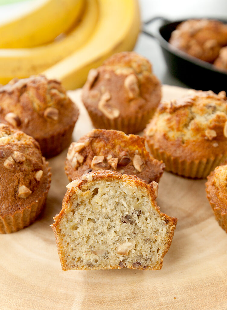 A wood plate with banana muffins, fried in the air fryer, with one sliced open to see the moist interior.