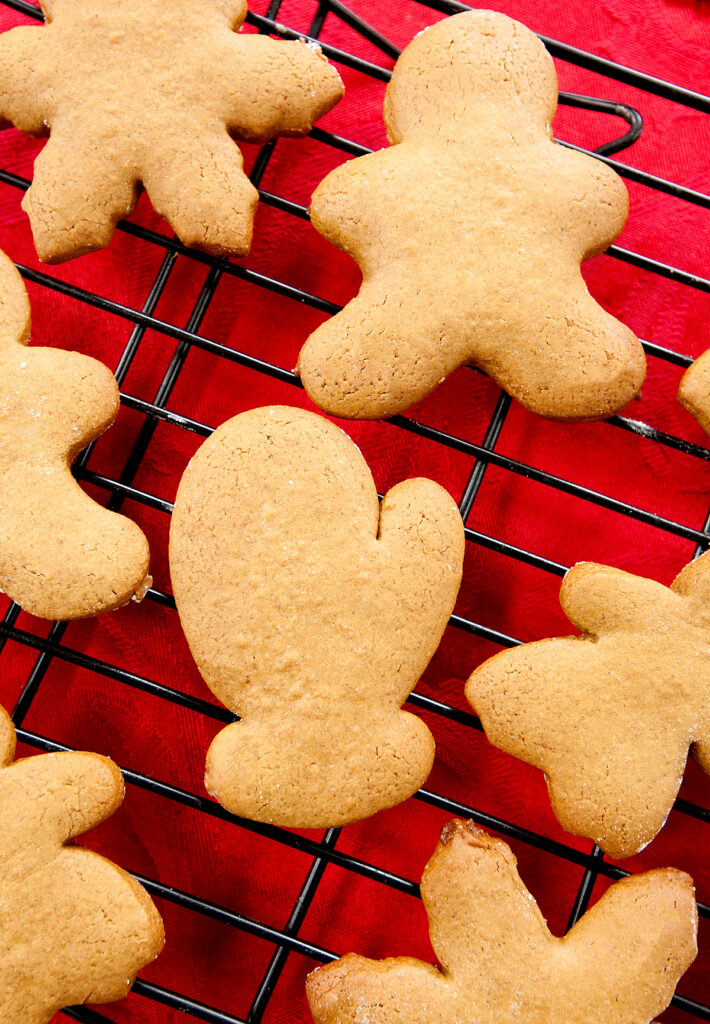 A close up of a mitten-shaped gingerbread cookie on a rack with other holiday shaped cookies.