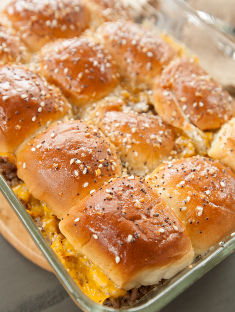 A pan of golden cheeseburger sliders fresh from the oven with glistening Hawaiian roll tops.